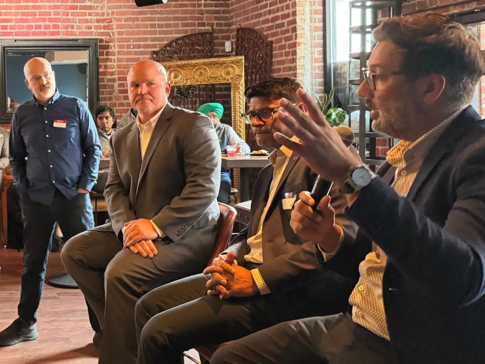 Panelists seated on a stage in a brick-walled venue, with one speaker gesturing while holding a microphone during a SaaSpocalypse discussion