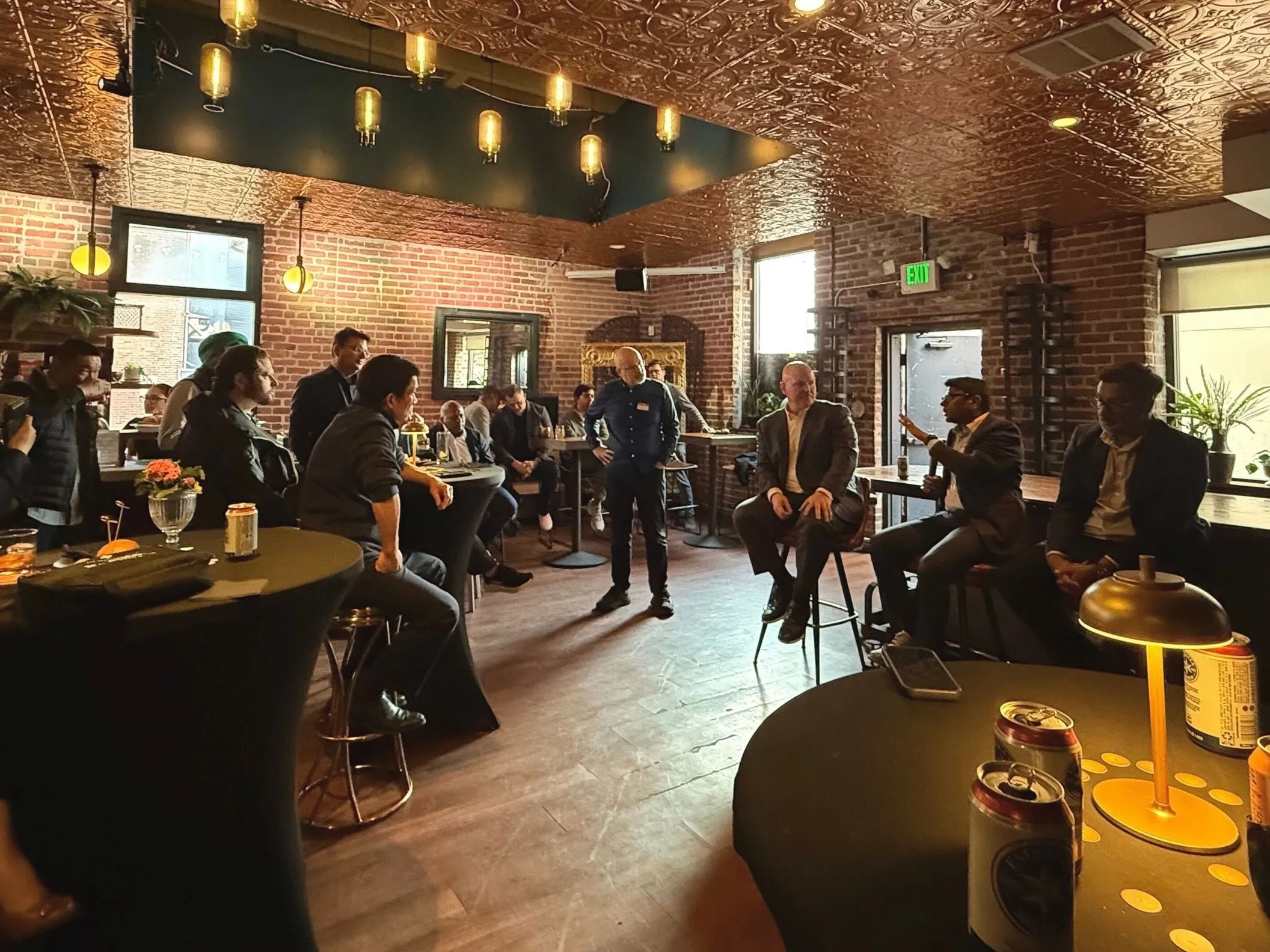 Wide view of the SaaSpocalypse venue showing attendees seated around the room while two panelists talk on a small stage between exposed brick walls
